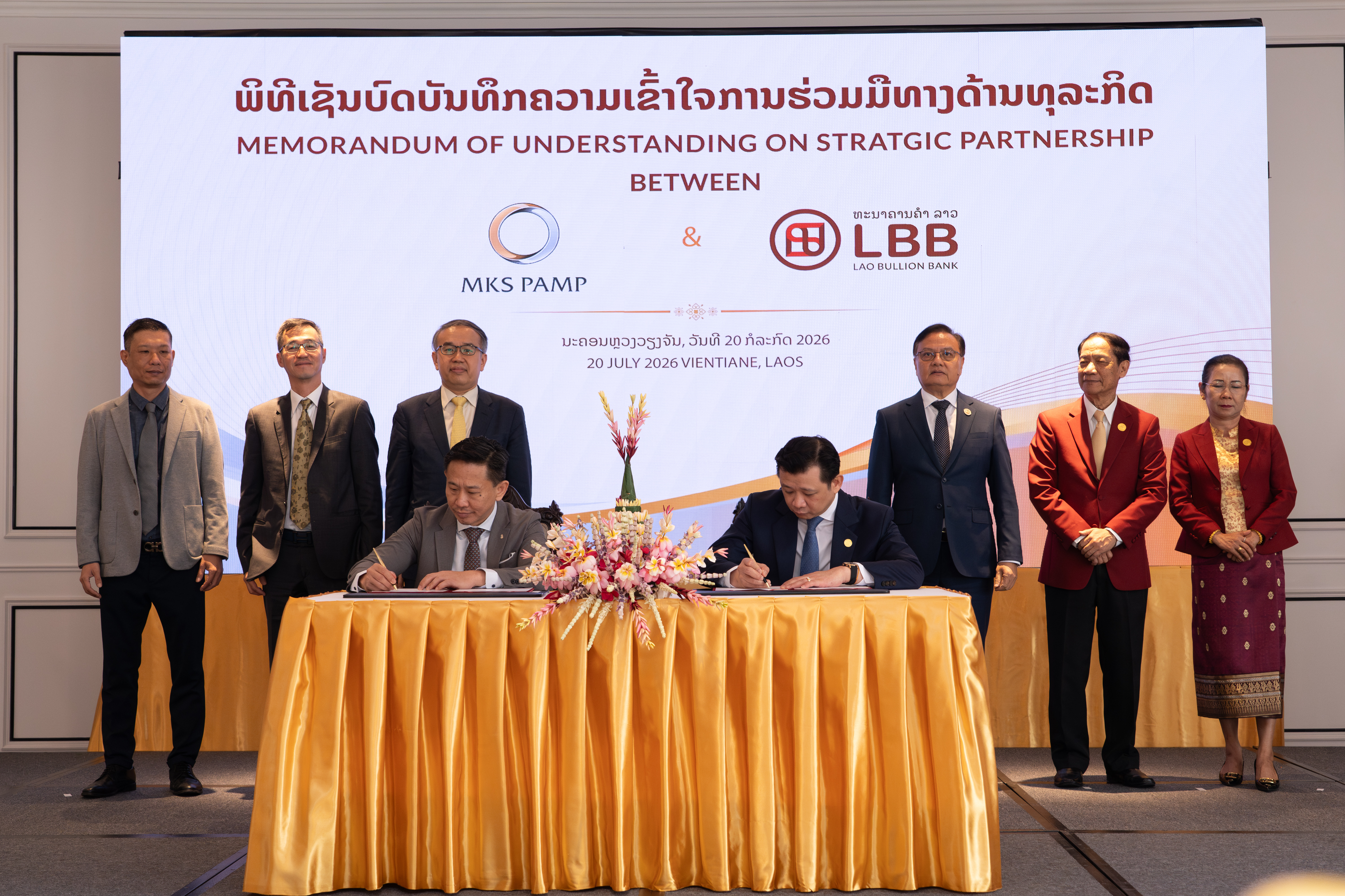 Mr. Santiphab Phomvihane, Deputy Prime Minister and Minister of Finance of Laos (back row, third from right), and Mr. Christopher Hui, Secretary for Financial Services and the Treasury of the Hong Kong SAR Government (back row, third from left), witness the signing of a Memorandum of Understanding on precious metals cooperation between Dr. Chanthone Sitthixay, Chief Executive Officer of Lao Bullion Bank (front row, right), and Mr. Damien Han, Head of Sales, Asia Pacific at MKS PAMP (Hong Kong) (front row, left).